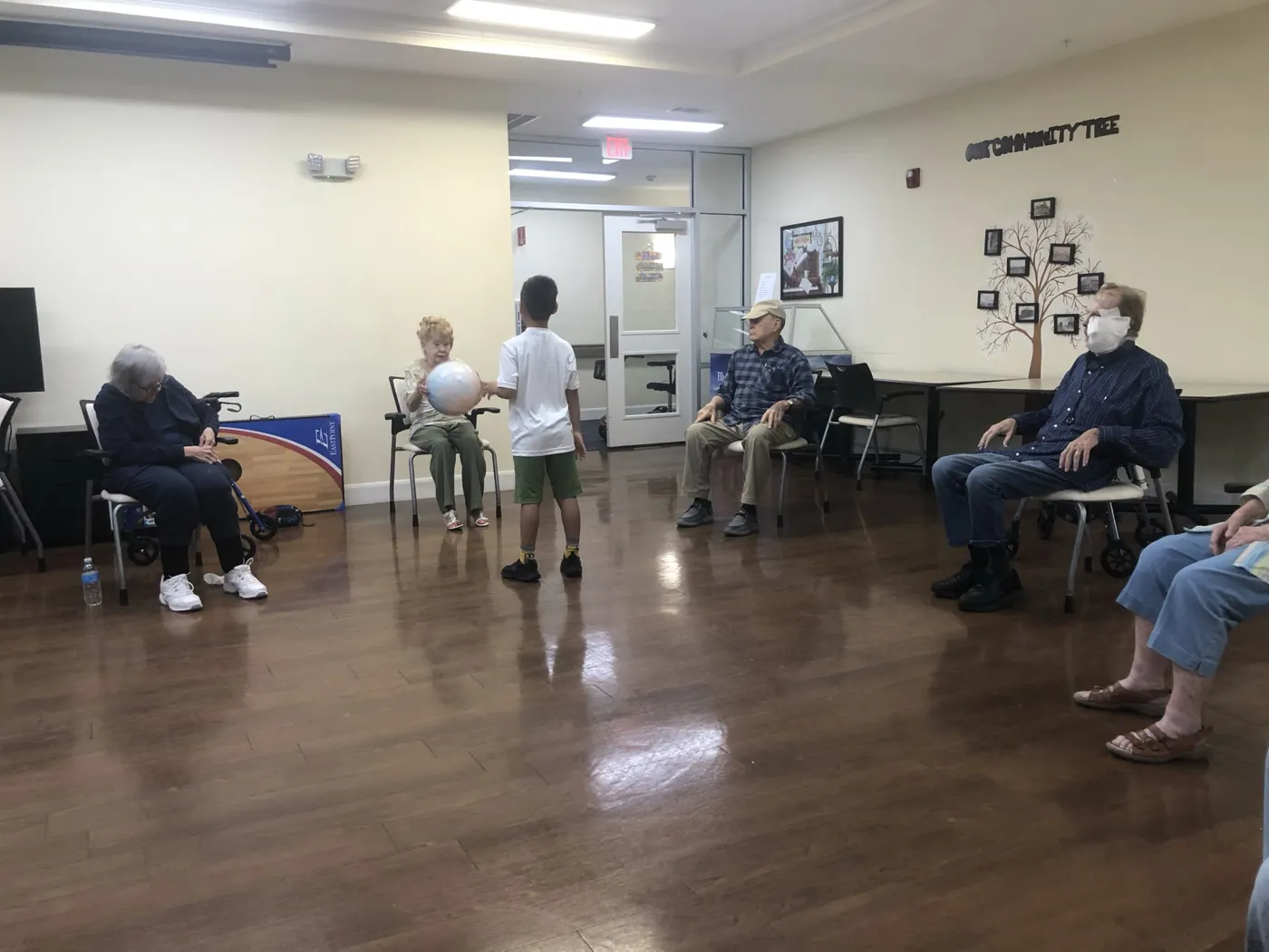Residents seated in a circle play a balloon game with a young volunteer in an activity room
