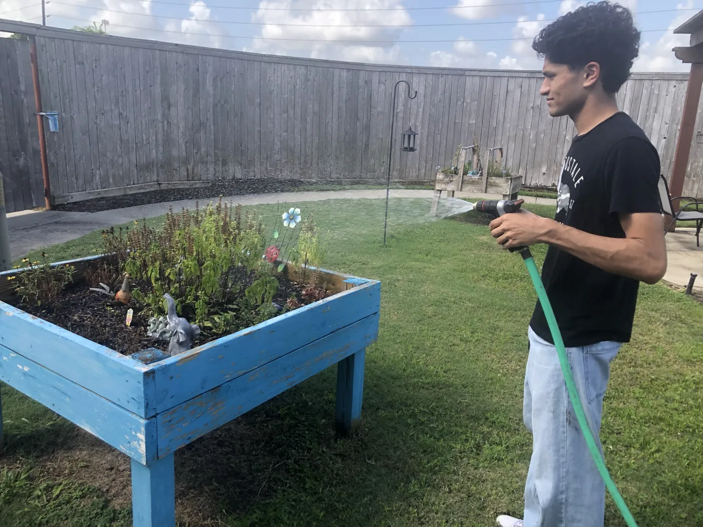 A volunteer waters a raised flower bed in a senior community's courtyard garden
