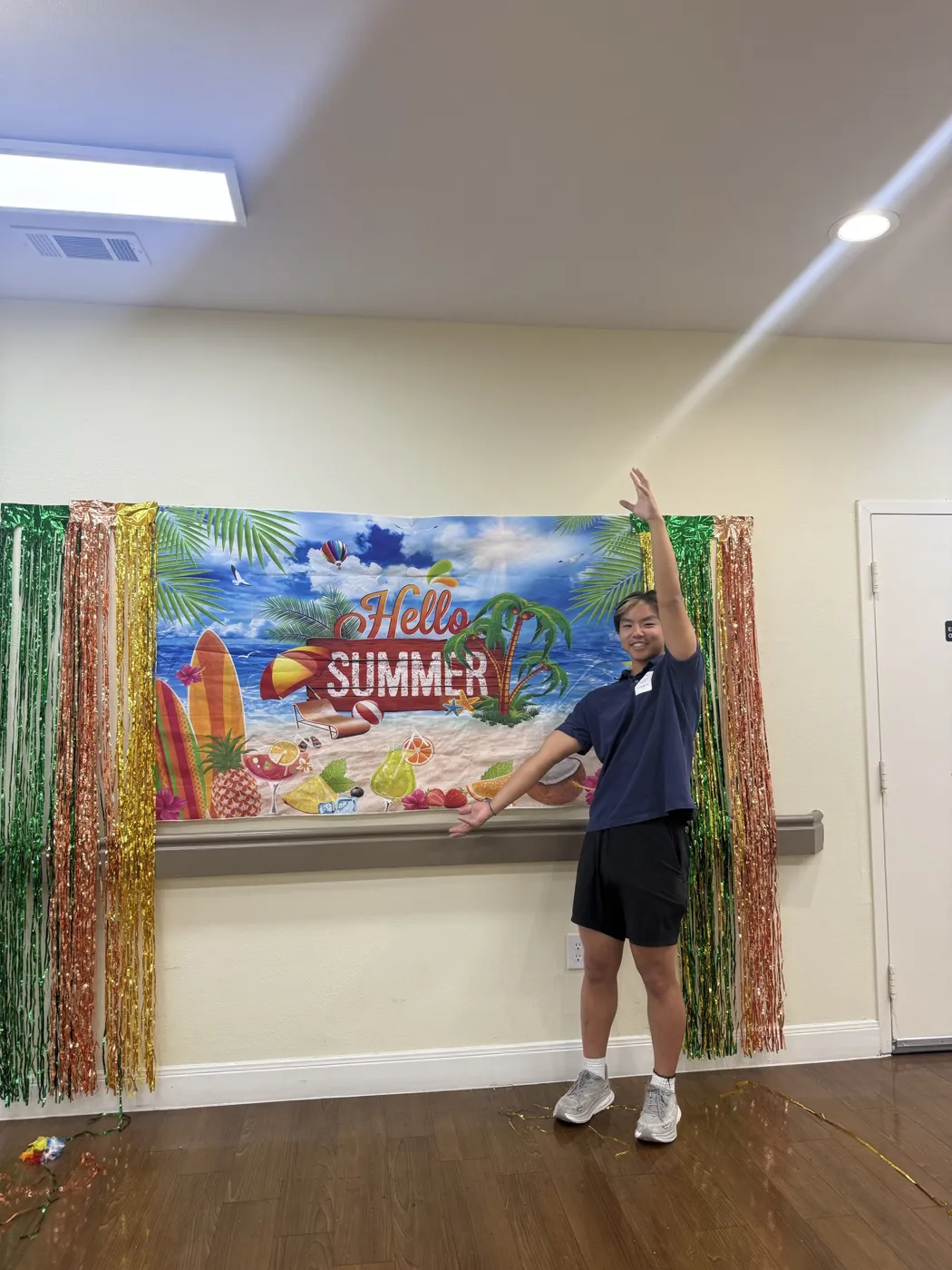 The founder of Senior Voices with arms raised in front of a Hello Summer backdrop at a partner community