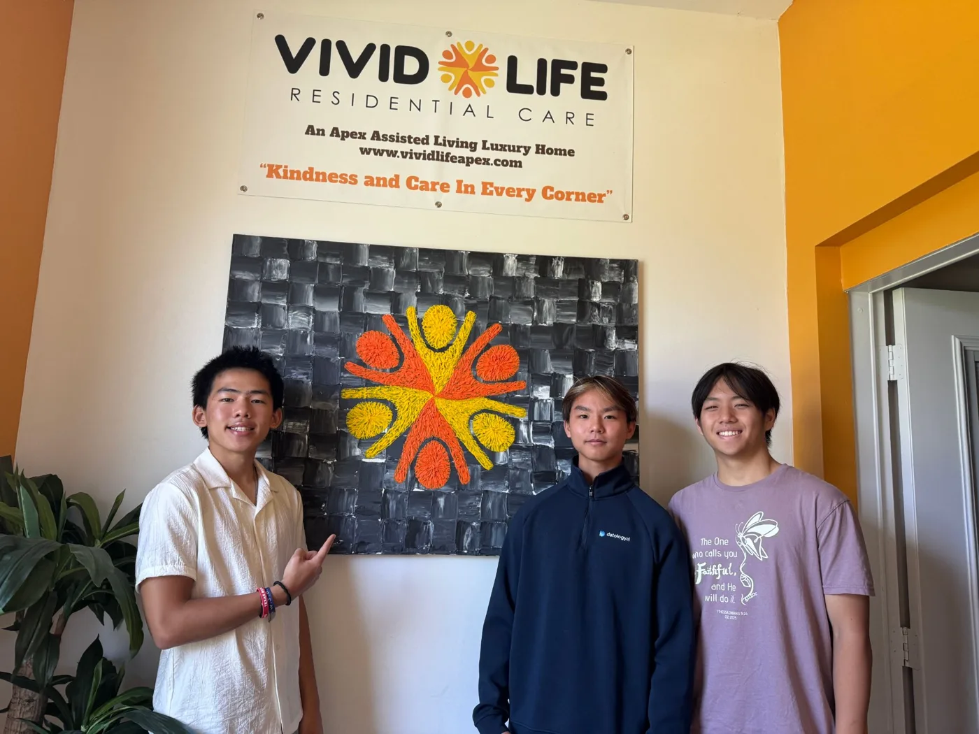 Three Senior Voices student volunteers smiling in the lobby of Vivid Life Residential Care, a partner community